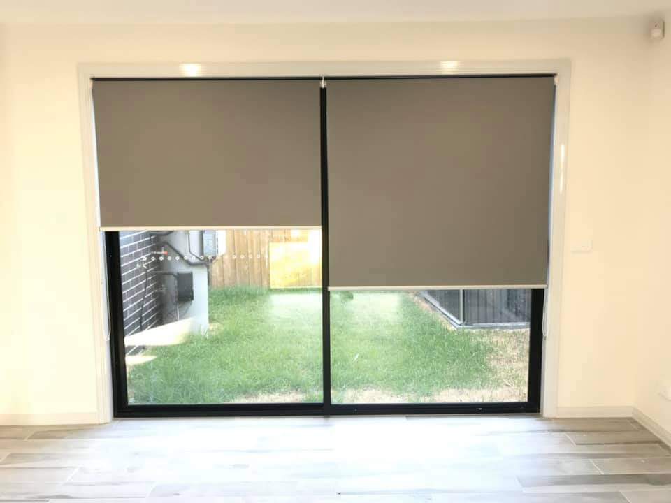 An image of a roller blind made from a white fabric material, covering a window. The roller blind is fully extended and mounted inside the window frame. The bottom of the blind is straight and even, with a thin metal bar that adds weight and stability to the fabric. The fabric is opaque, blocking out most of the natural light and providing privacy for the room. The cord mechanism used to raise and lower the blind is visible on the right-hand side, with the cords hanging down in a neat loop. The roller blind has a sleek and minimalist design that blends in with the window frame and walls, creating a clean and modern look