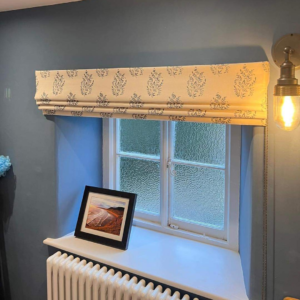 Alt text: A close-up view of a Roman blind in a neutral color. The blind is made of a smooth fabric and features horizontal folds when raised. It covers a window, providing privacy and light control